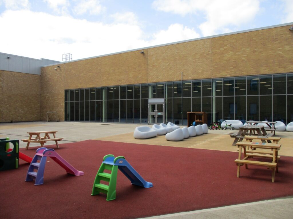 Photograph of the outdoor visits space, featuring some play equipment for children, picnic tables, and some plastic garden furniture.