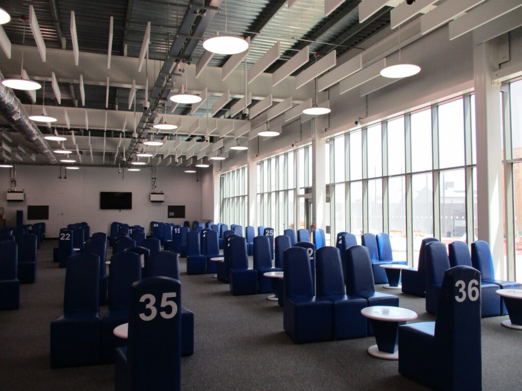Photograph of the interior of the visits hall, with sets of chairs clustered around low tables. Each set has a number painted on the back of one of the chairs in it.