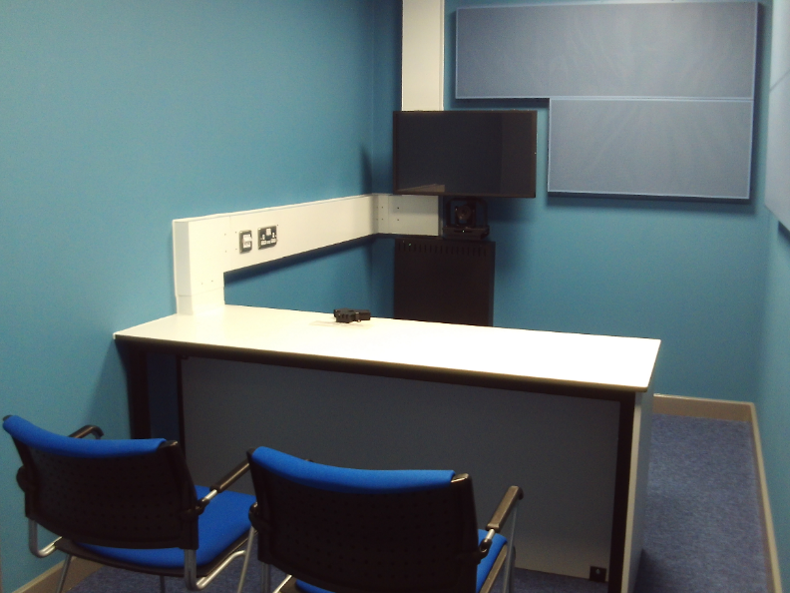 Photograph of the video conferencing suite for legal visits. There is a desk, two chairs and a TV mounted on the wall opposite them.
