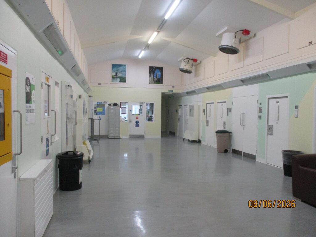 Photograph of the segregation unit, a wide corridor with doors off both sides with posters and information displayed on the walls.