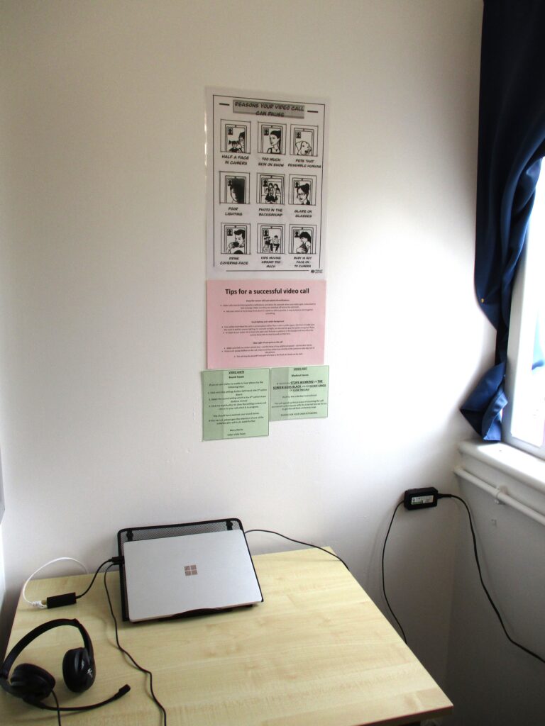 Photograph of a secure video calling facility, a small room with a laptop on a stand with a pair of headphones.