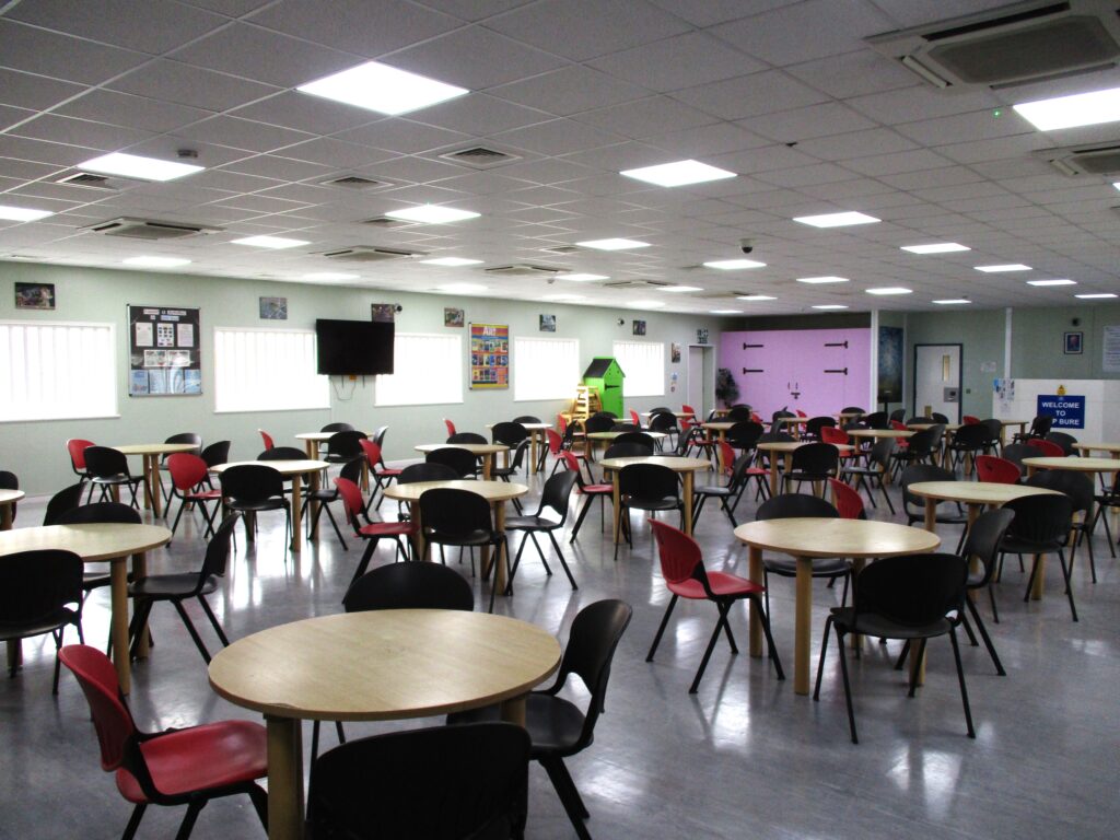 Photograph of the visits hall, a long room with chairs arranged around rows of circular tables.