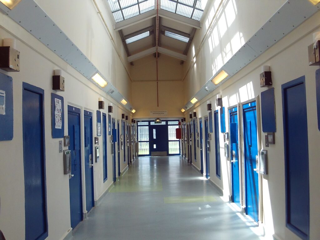 Photograph of the segregation unit, in which a corridor with a pitched ceiling can be seen. Doors to cells are on both sides of the unit.