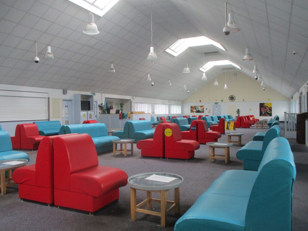 Photograph of the visits hall at HMP Lindholme. Chairs are arranged around tables in rows. The chairs are covered in red and blue fabric.