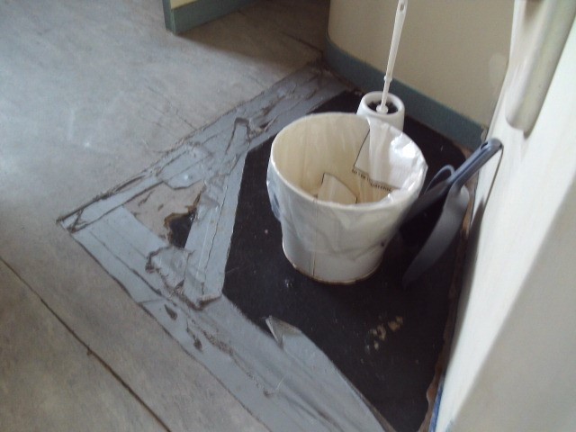 Photograph of broken cell flooring that needs repair on a residential unit.