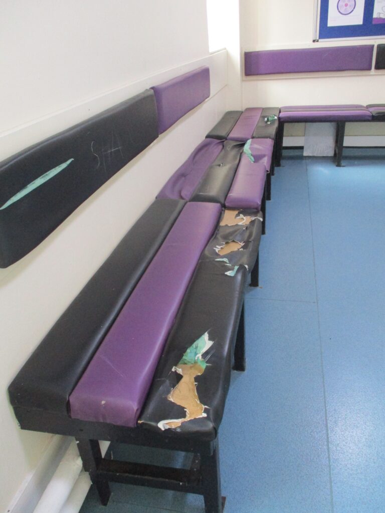 Photograph of a seating area in a waiting room showing damage to the upholstery of one of the benches.