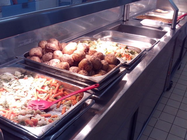 Photograph of a food servery counter, with several foods in metal trays ready to be dished up.