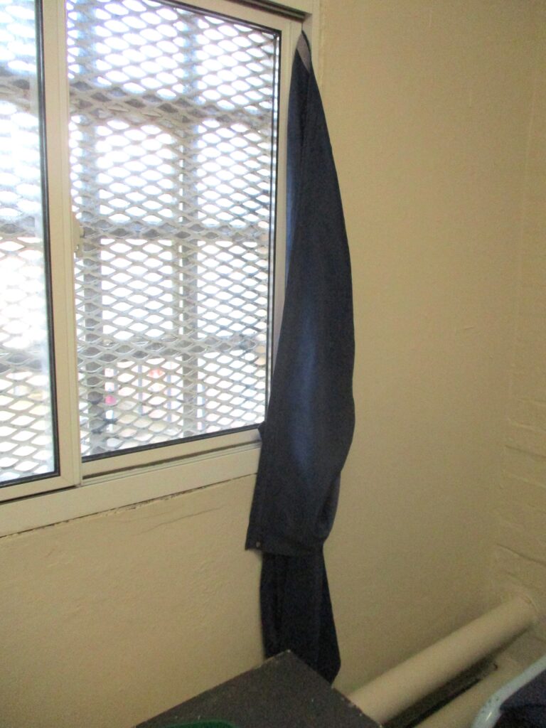 Photograph of a curtain hanging off one corner of a curtain rail, a potential ligature risk.