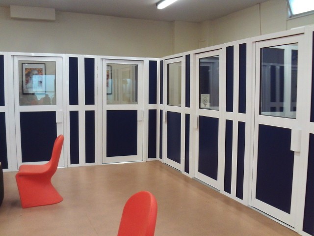 Photograph of legal visits booths in the visits hall. The doors to the booths are are white and navy blue in colour, with glass panels in their upper halves.