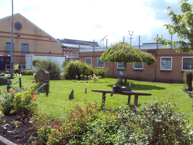 A picture of the outside areas, showing a grass area with shrubs and trees in front of some low buildings.
