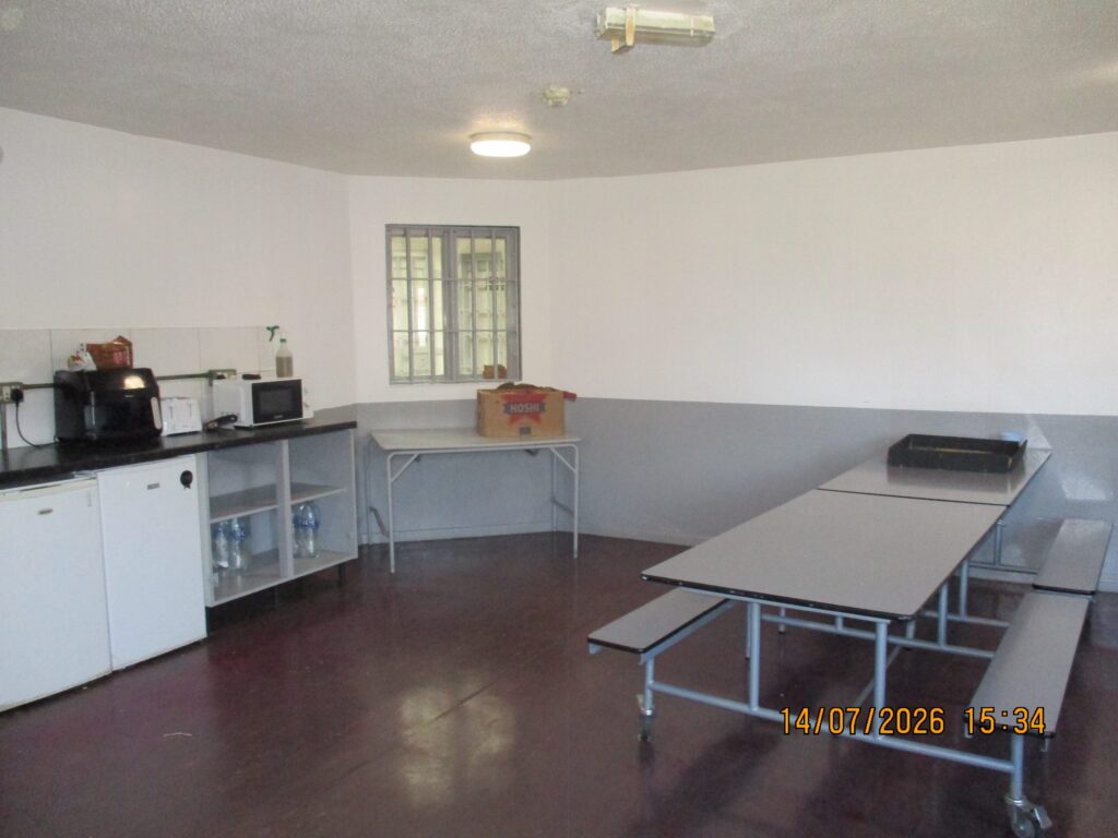 Photograph of an association room, with tables and benches to one side and a kitchenette to the other. Basic cooking equipment can be seen on one of the counters.