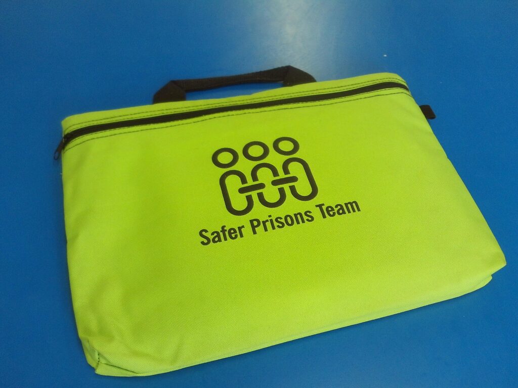 Photograph of a document bag with a logo and the words 'Safer Prisons Team' printed on it. the bag is a shade of lime green.