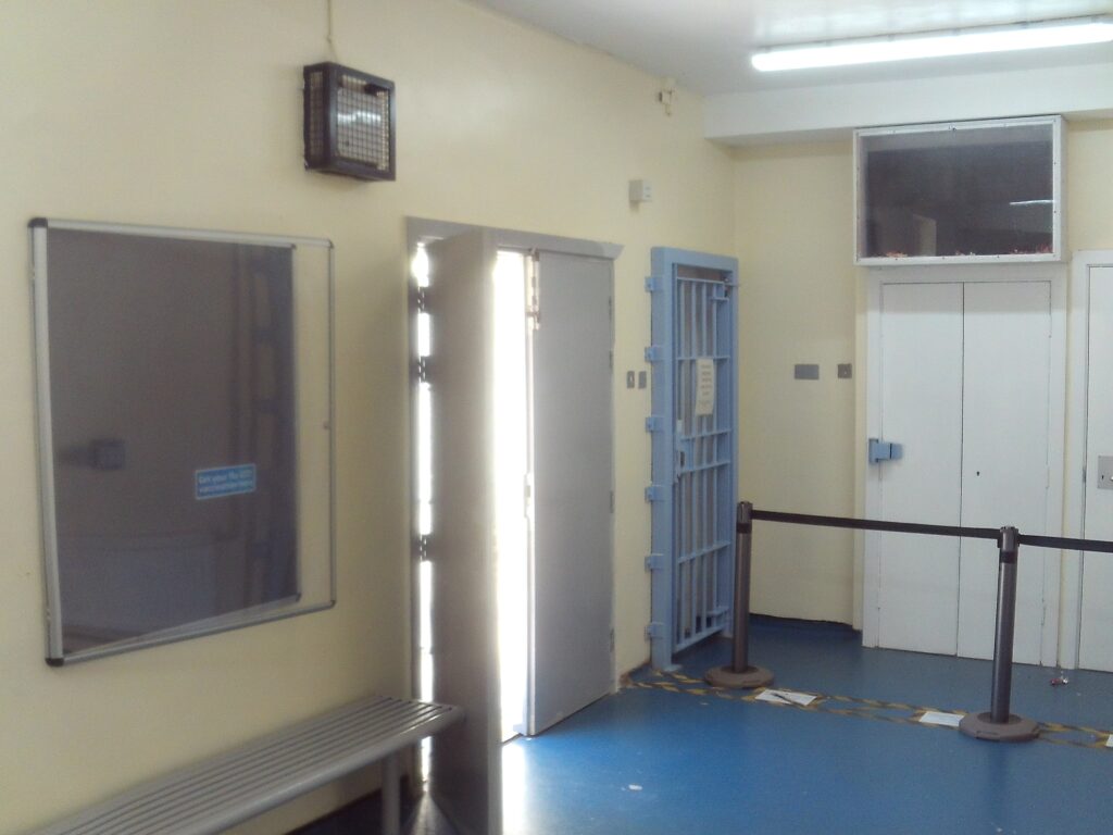 Photograph of a patient waiting area. the outside door is open and there is a bench against one wall.