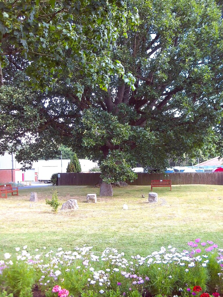 Photograph of the pagan circle, an area of grass with a stone circle in it. Trees, flowers and benches can be seen around the edge of the circle.