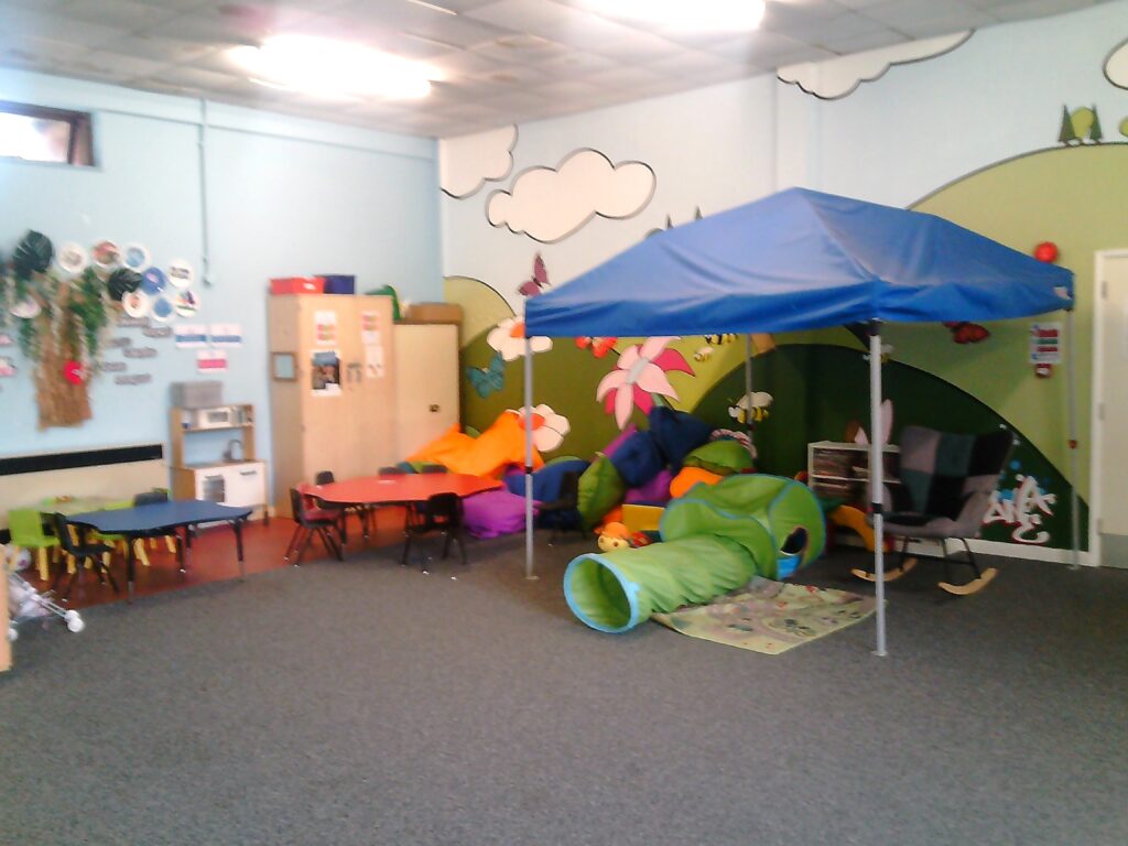 Photograph of the children's area in the visits hall, a corner with a decorative wall painting and a variety of toys and games arranged against the walls ready for use.