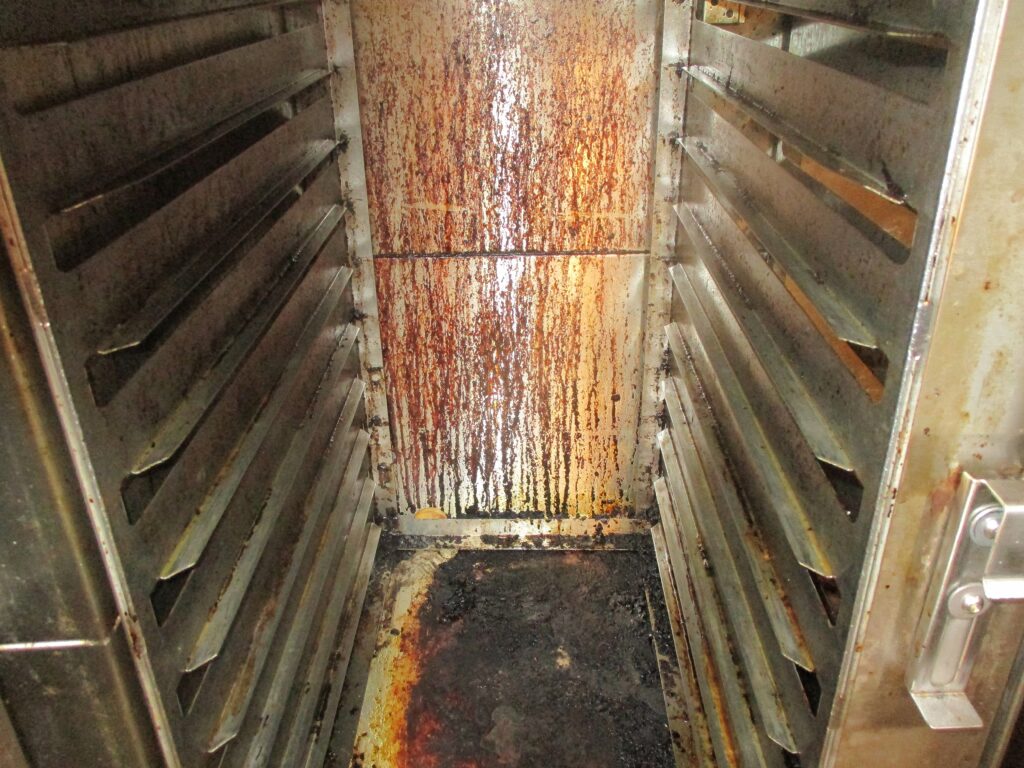 Photograph of a grimy food trolley. The close-up shot of the inside of the trolley shows it is covered in dirt and grime on the back, base and sides.