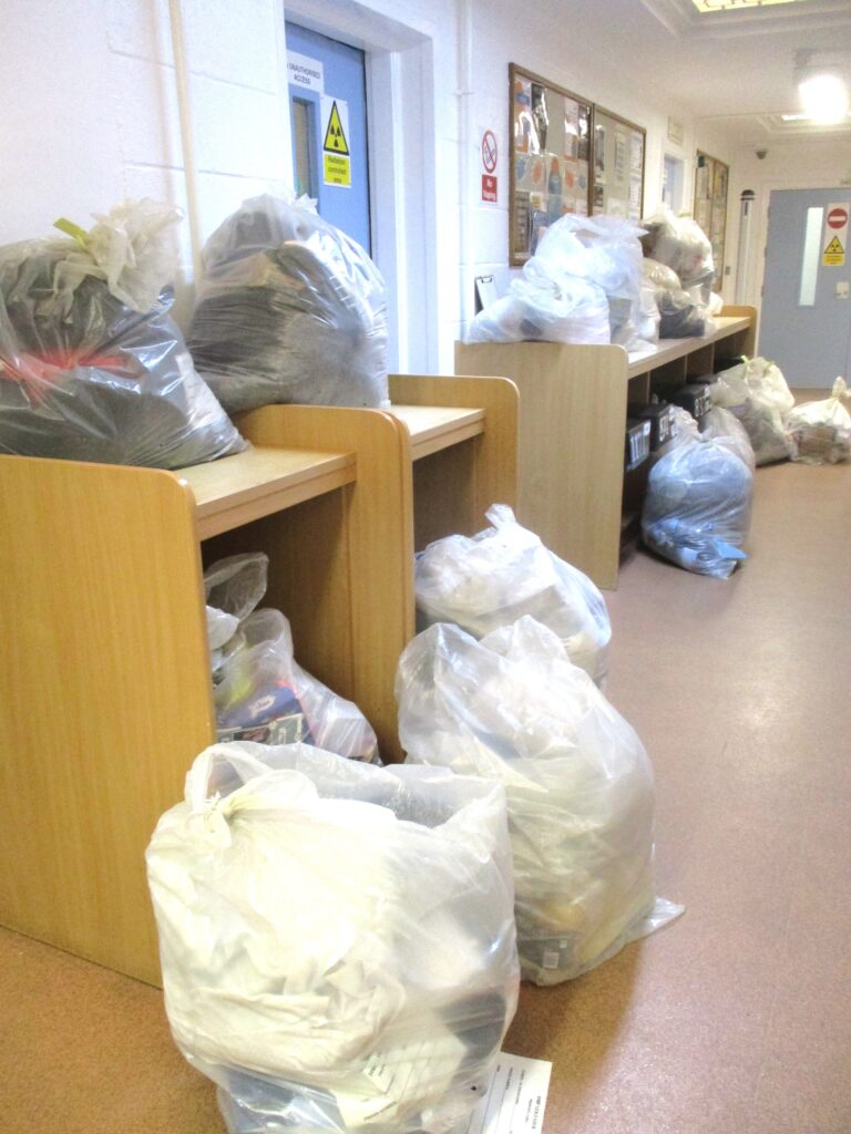 Photograph of bags of prisoners' belongings on tables and the floor along the length of a corridor.