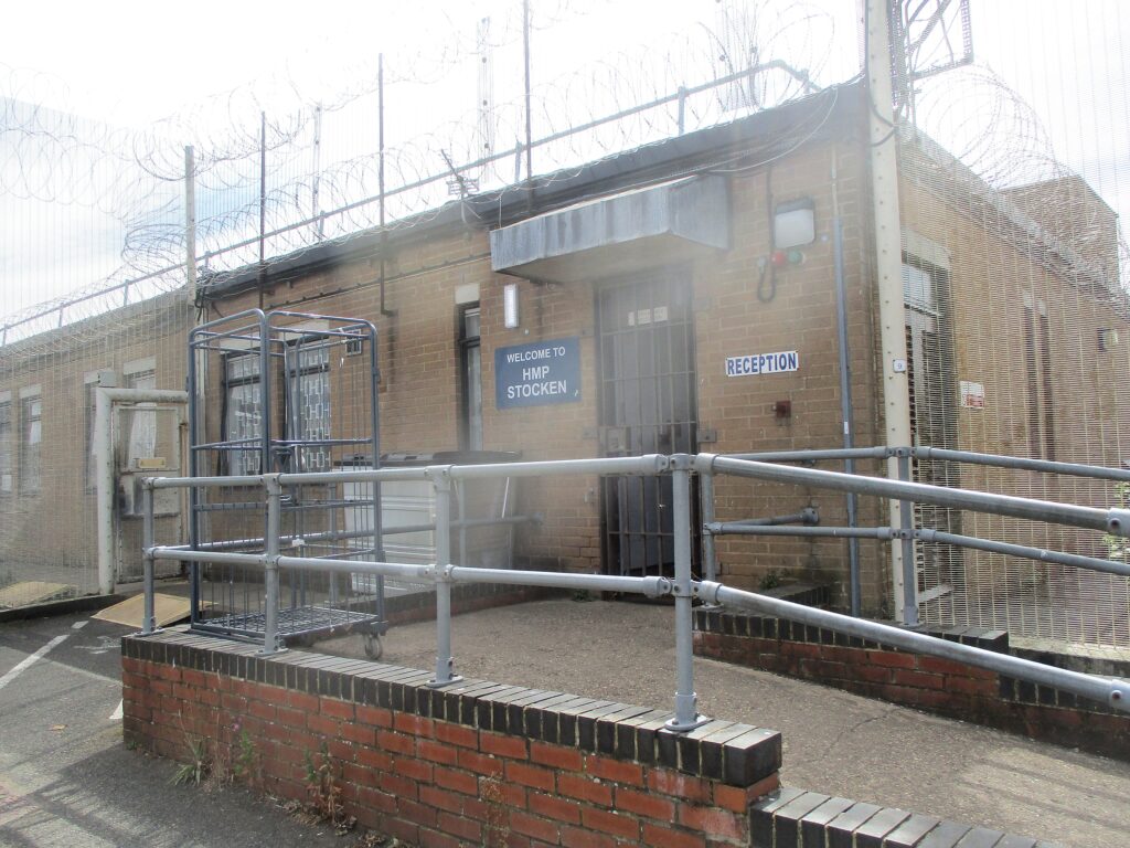 Photograph of the entrance to reception. A concrete and brick construction ramp leads up to the door of a one-storey building. Outside the door there is a welcome sign on the wall.