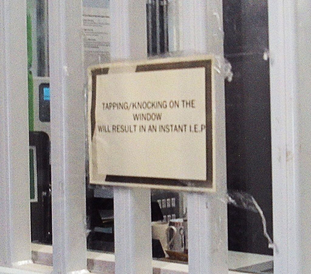 Photograph of a printed sign stuck on the bars of an office warning prisoners that tapping or knocking on the window will result in an instant LEP.