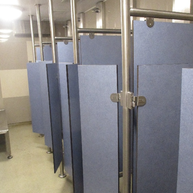 Photograph of shower cubicles, showing rows of blue privacy-stall partitions, stainless-steel support poles, and overhead lighting.