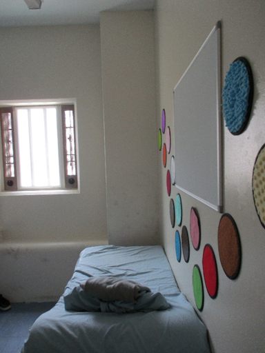 Photograph showing constant supervision cell two featuring a neatly made bed, window, and white wall panel surrounded by colourful circular decorations.