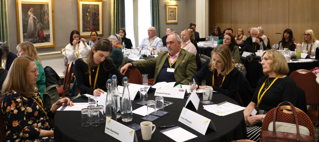 Photo of attendees at the NPM conference sitting at tables during a presentation.