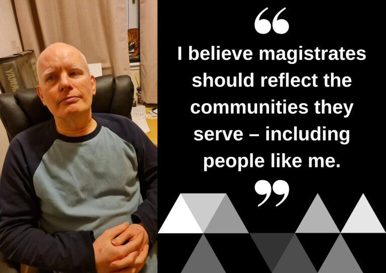 A man is sat in casual clothing in an office chair with his hands clasped together.