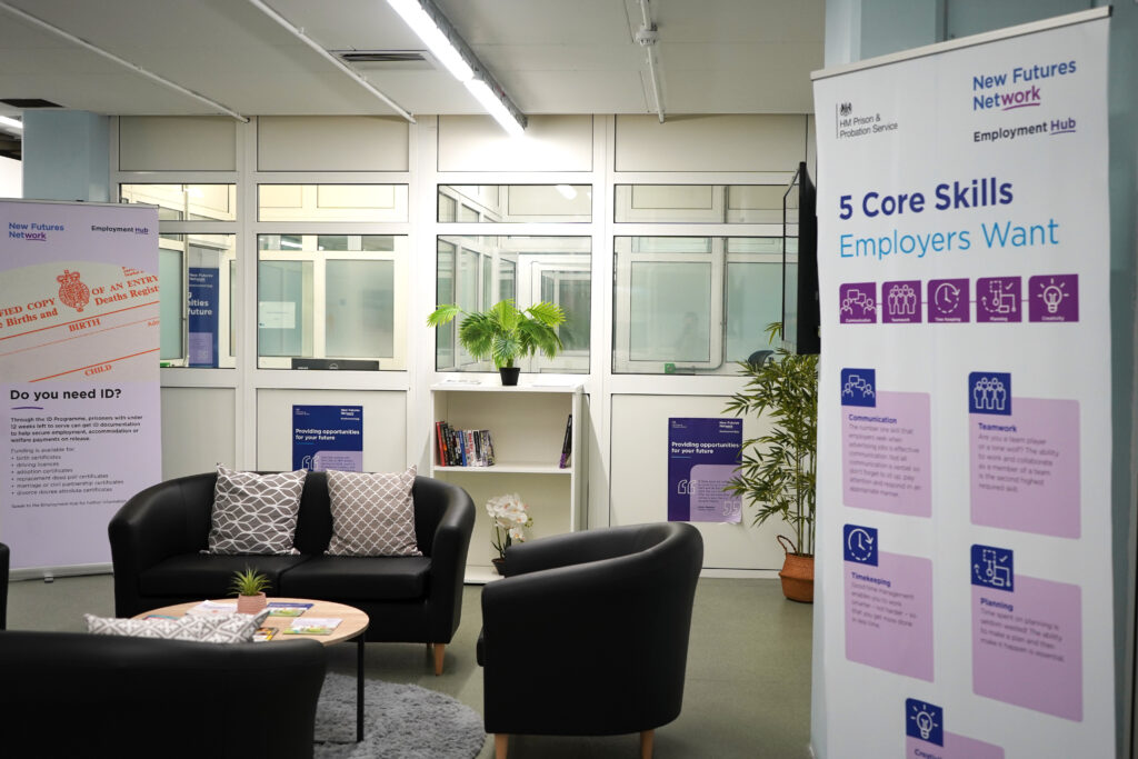 A prison Employment Hub furnished with a small bookcase, two potted plants, two pull up banners, two sofas and an armchair.