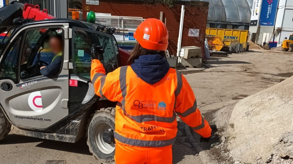 A lady in personal protective equipment directing a vehicle on a construction site.