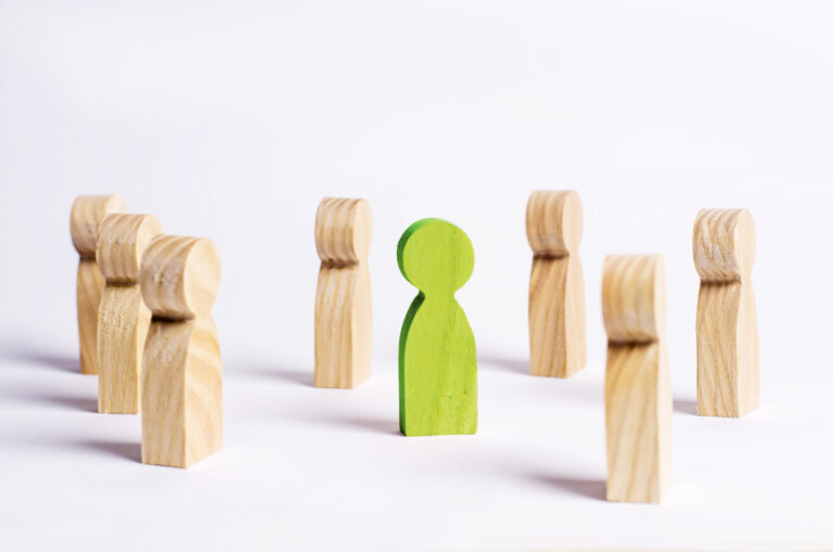 Image of 7 wooden figures surrounding one green wooden figure in the middle. The background is plain white.