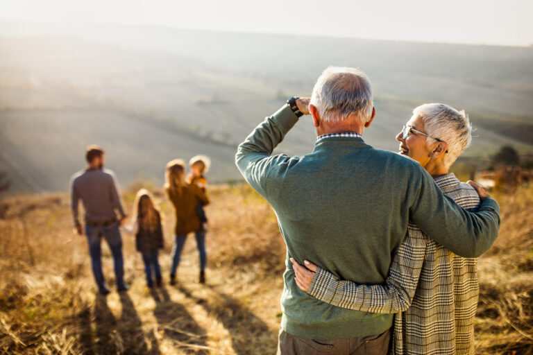 An older couple, facing away from the camera, look down a hillside path towards a younger couple walking with young children.