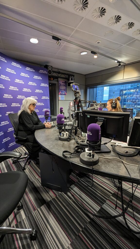 Baroness Newlove being interviewed in BBC Radio Manchester radio studio, with station branding in the background. 
