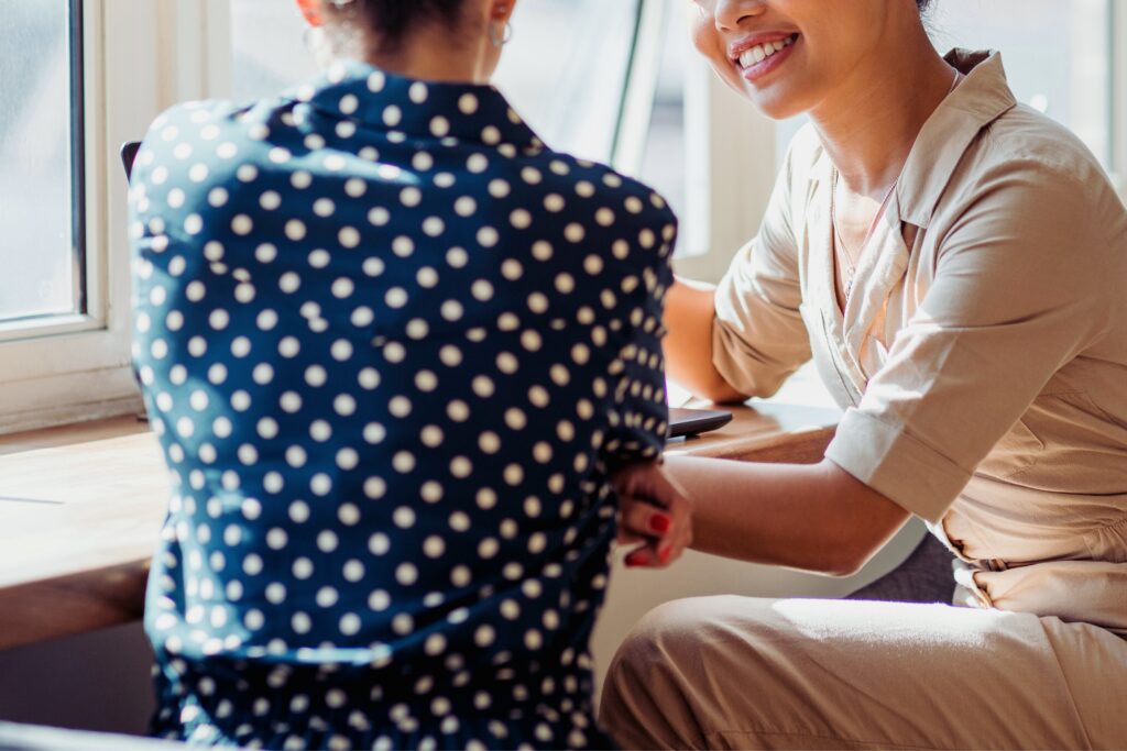 Image showing 2 people having a work meeting and chatting, one is smiling and looking at a laptop