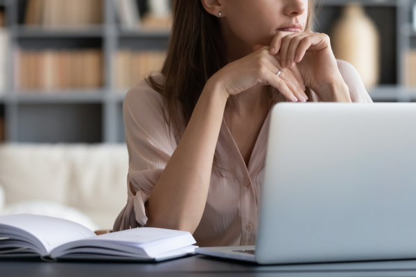 Image of a woman sitting at a desk with a laptop in front of her, thinking.