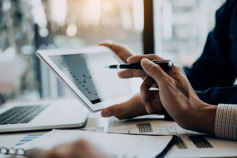Photo of hands holding a tablet which displays a graph. Second hand holding pen pointing to the screen.