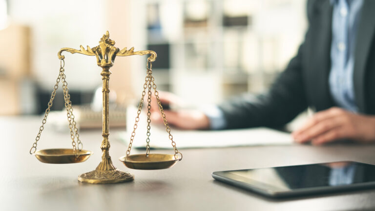 Image of justice scales on a desk, in front of a man writing on a piece of paper
